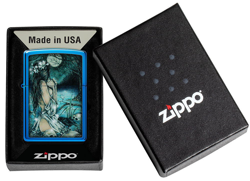 Zippo aansteker glanzend blauw in mystiek landschap met licht geklede dame aan het meer omringd door doodshoofden en kraaien in open doos